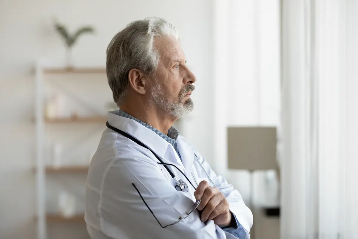 A man with a stethoscope standing in front of a window.