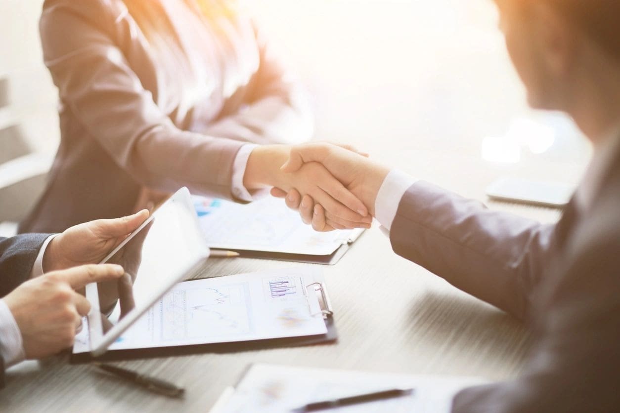 Two people shaking hands over a table.